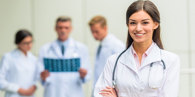 Imagem de uma médica sorrindo em primeiro plano e outros profissionais de saúde ao fundo desfocado